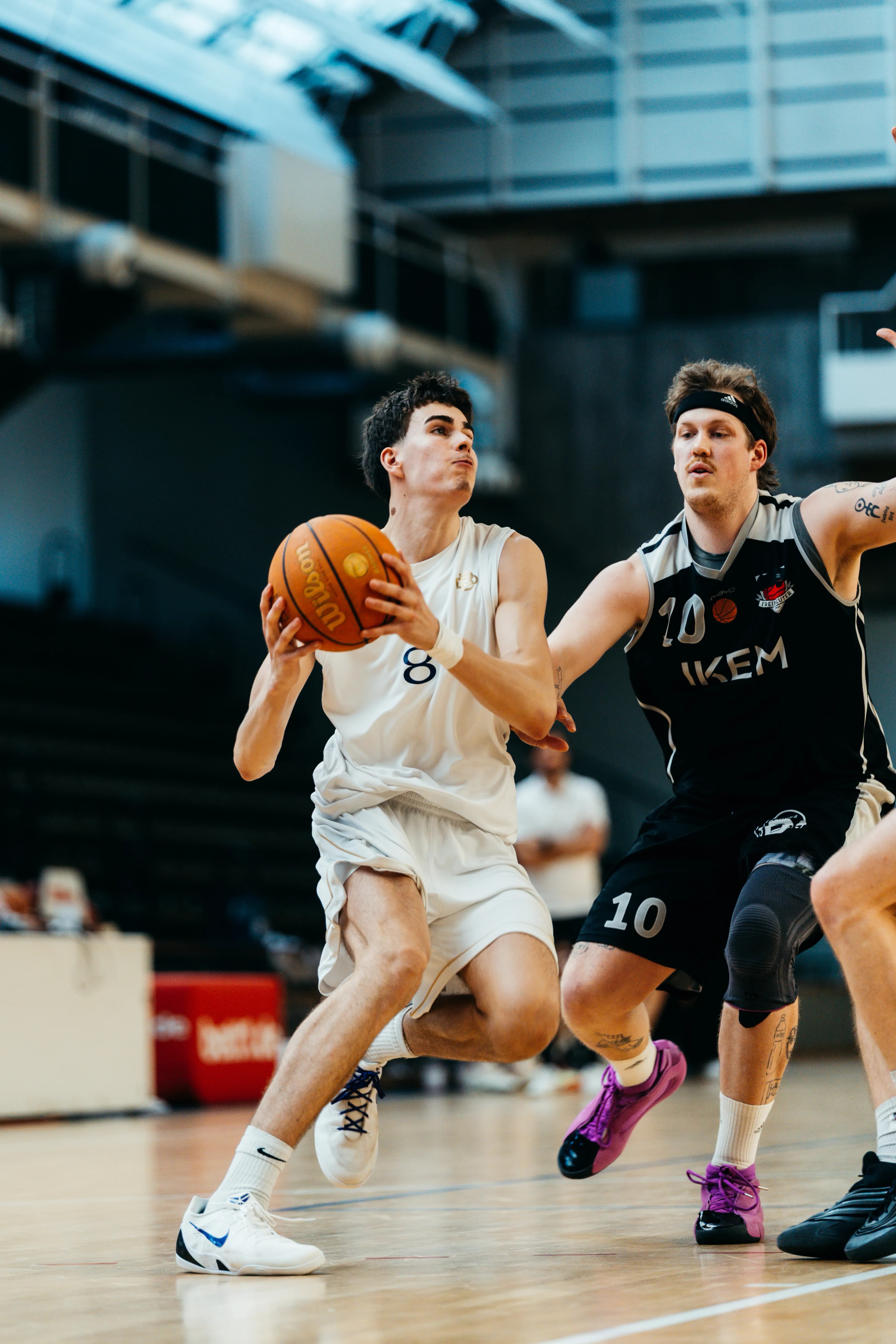 Player in white number 8 driving to the basket, defender in black number 10 contesting