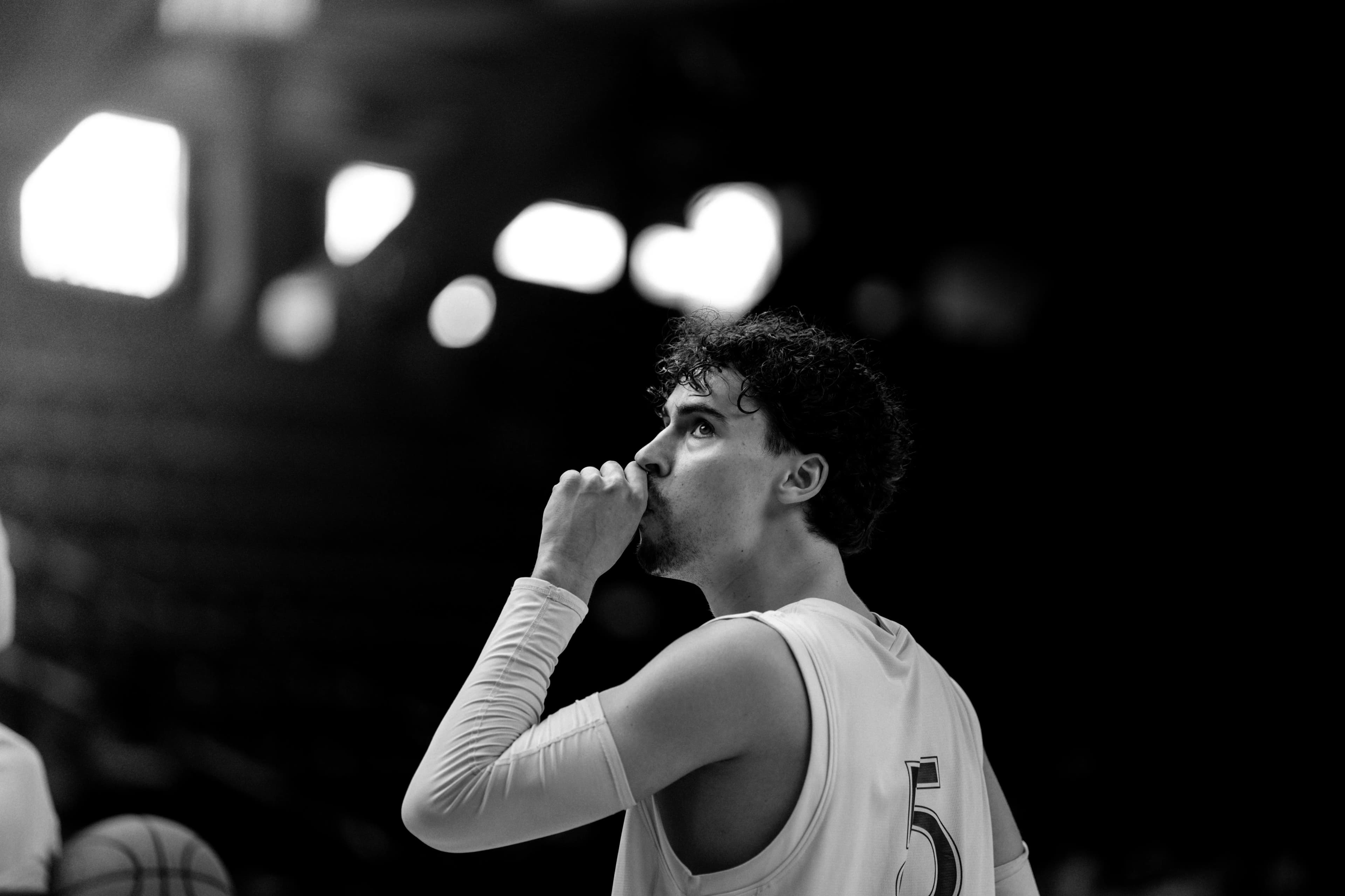 Black-and-white portrait: basketball player number 5 with a compression sleeve looking upward in the arena