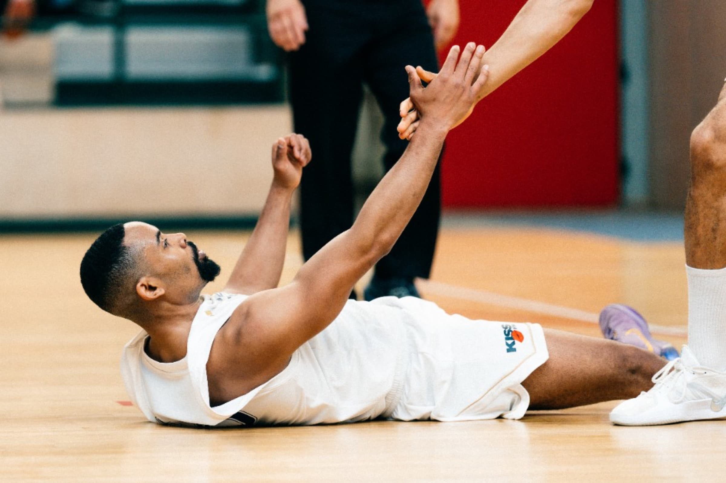 Player lying on his back on the court reaching up to take a teammate’s hand
