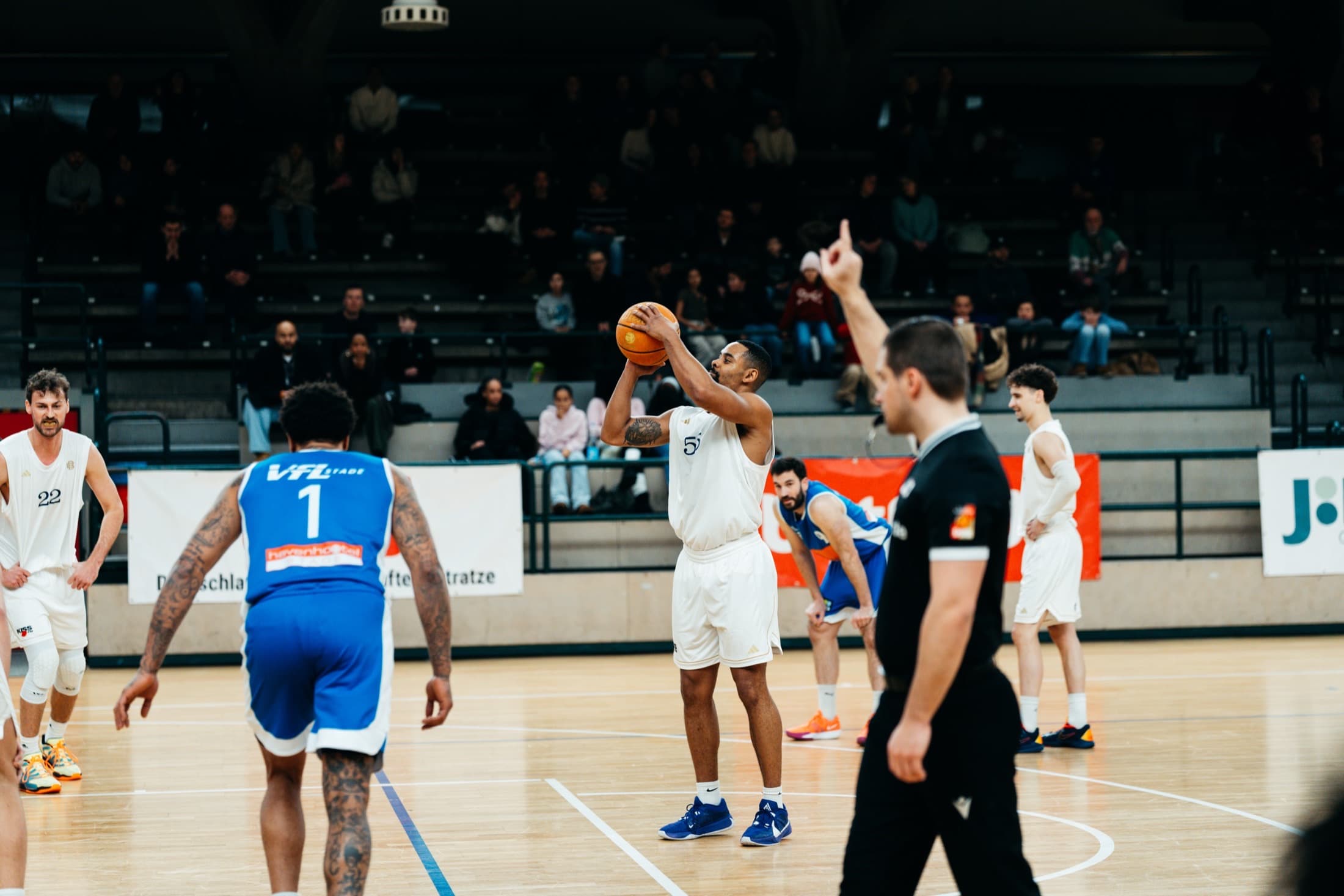 Player number 5 shooting the ball overhead, referee signalling, VfL Stade opponent in the foreground