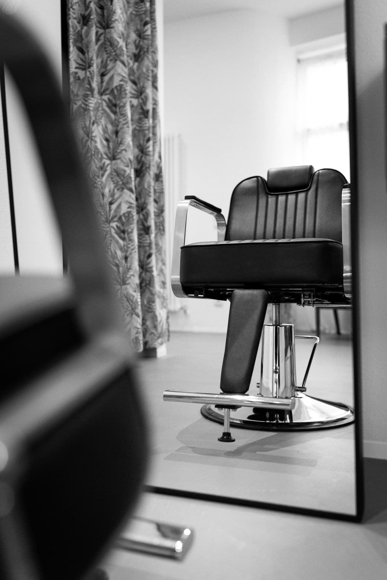 Black and white: mirror reflection of a black styling chair with chrome base and palm-leaf curtain in the salon