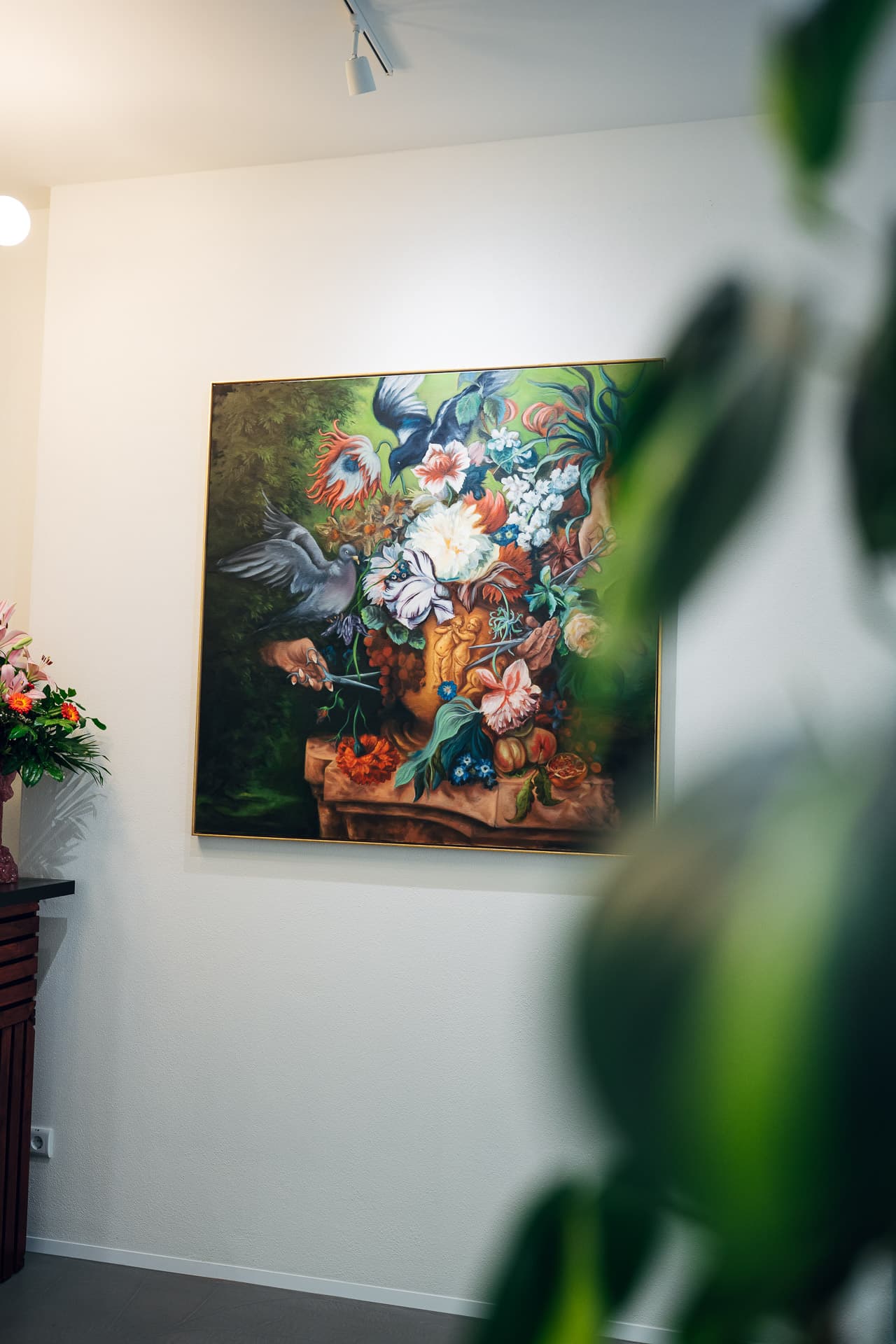 Large floral still-life painting on the salon wall, real lilies and a plant in the foreground