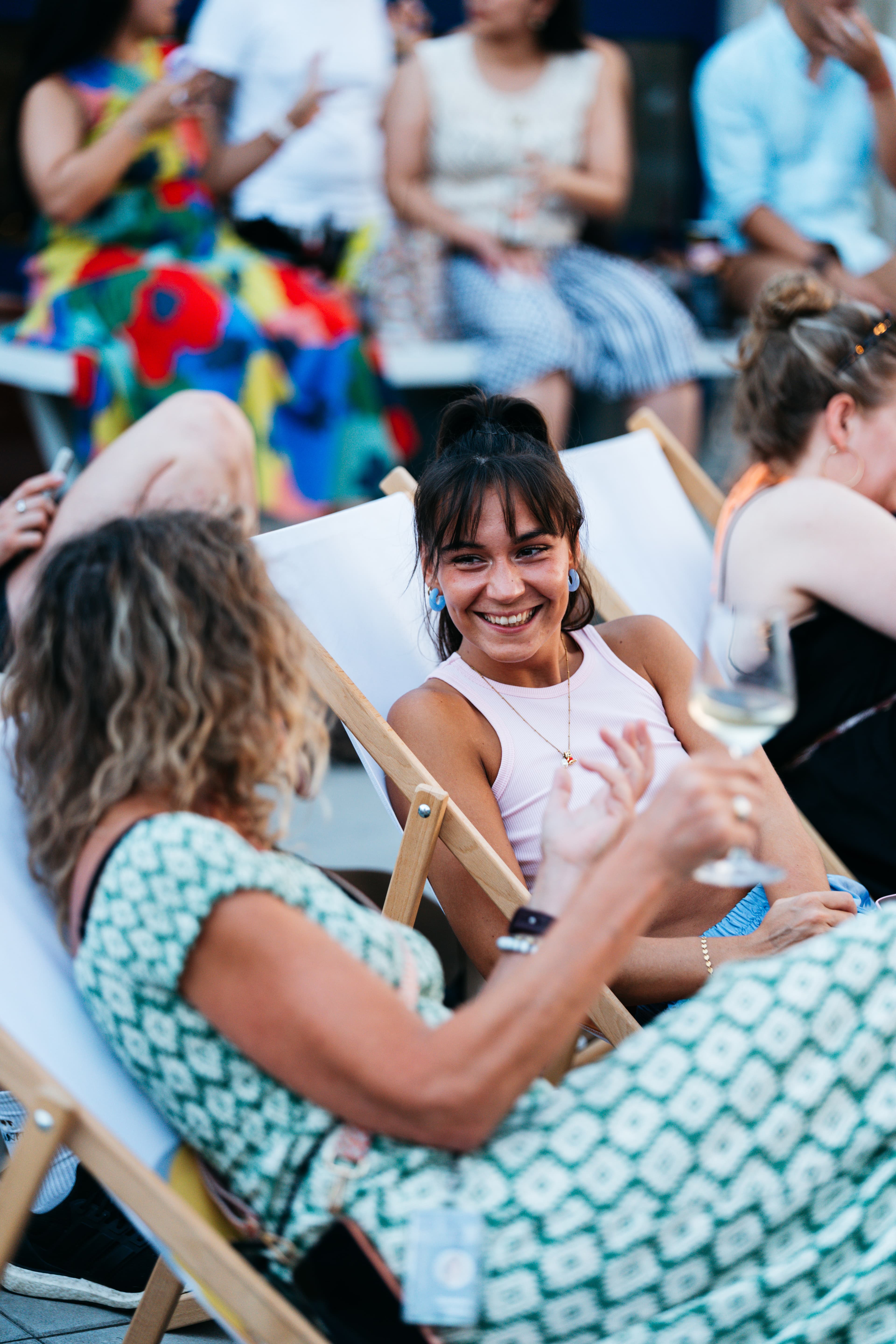 Two women in deck chairs smiling and talking over wine at rooftop office