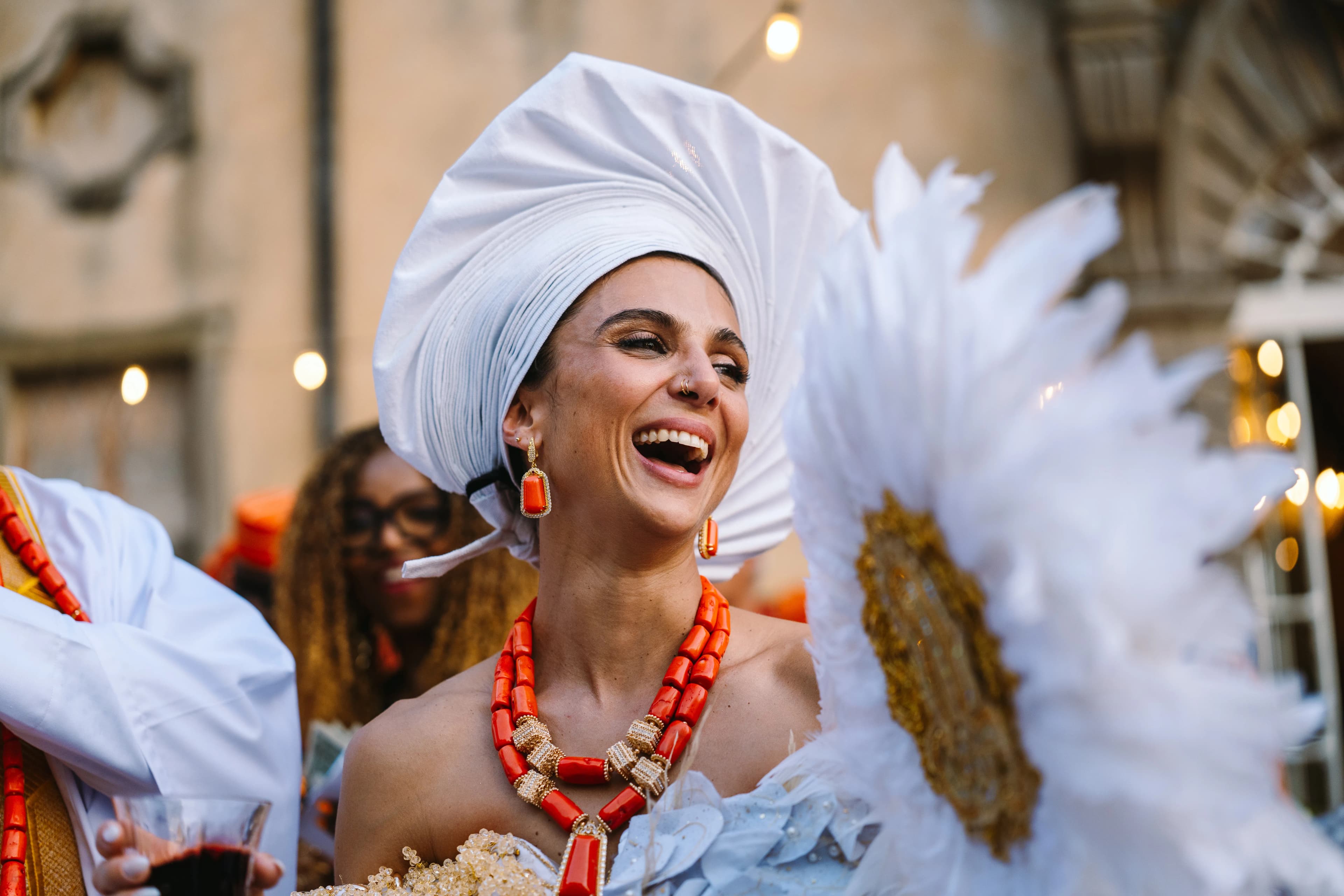 Bride in a white headwrap and coral jewellery laughing at Isa and Madu’s wedding